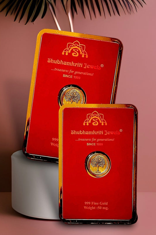 Two red Shubhamkrih Jewels gift boxes with gold trim, each featuring a circular gold coin insert, displayed on a pink background with a white cylindrical pedestal and decorative leaves.
