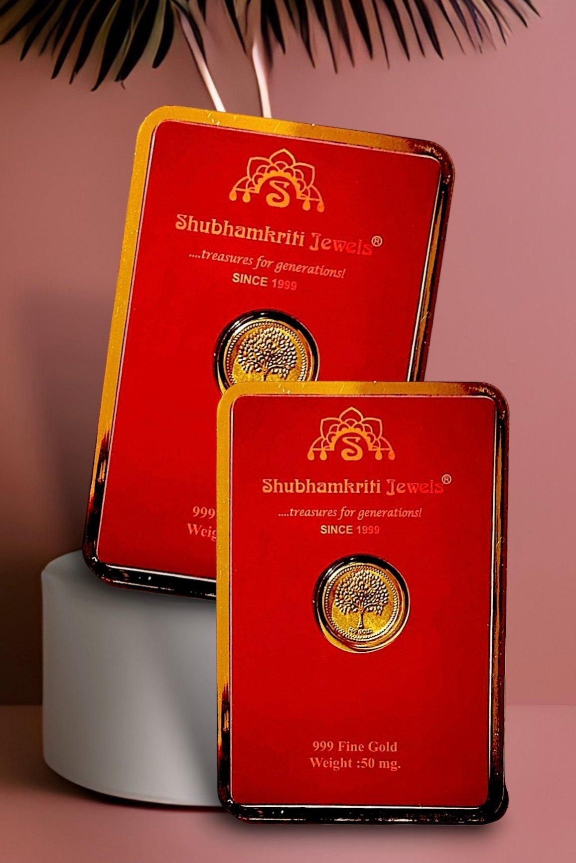 Two red Shubhamkrih Jewels gift boxes with gold trim, each featuring a circular gold coin insert, displayed on a pink background with a white cylindrical pedestal and decorative leaves.